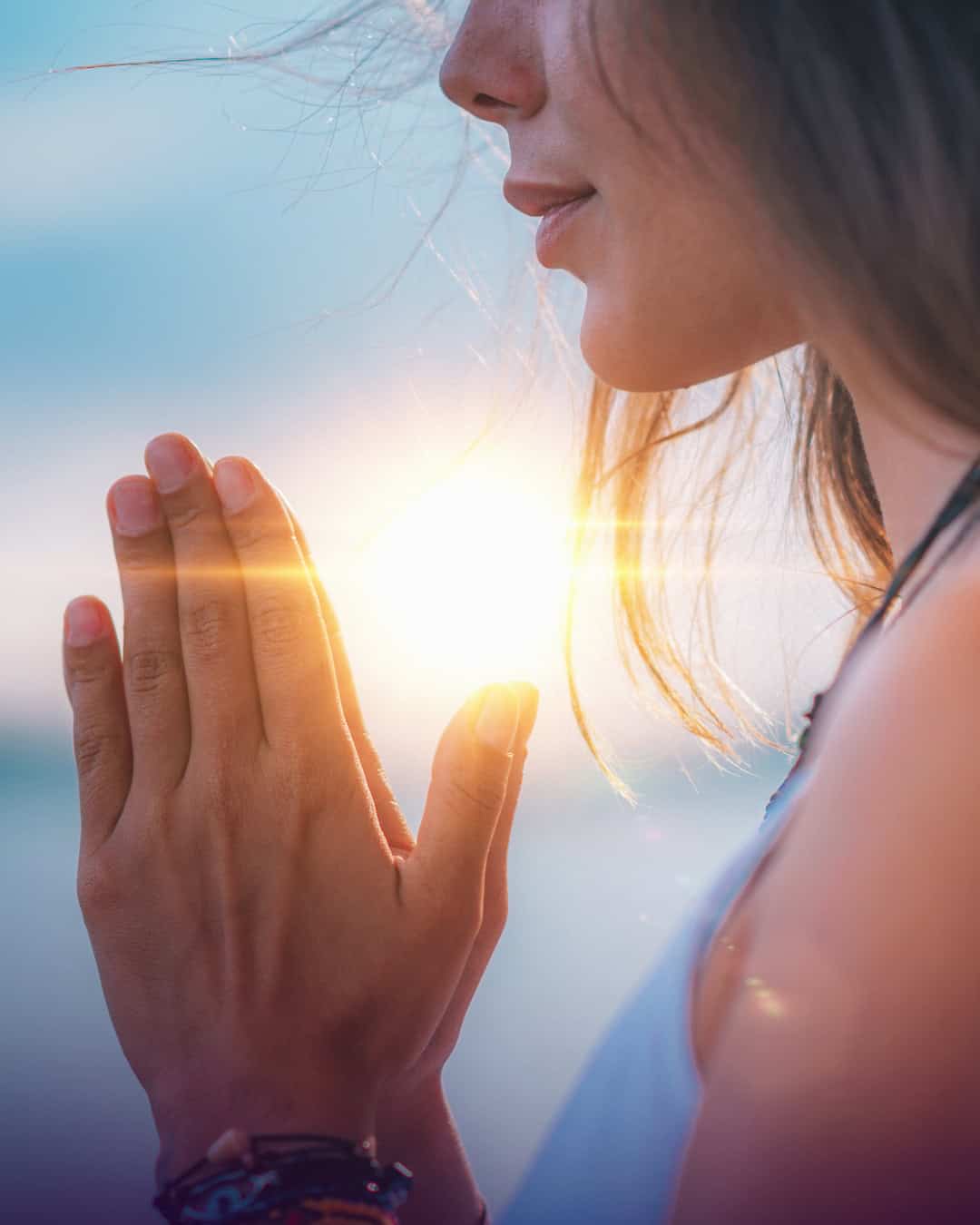 A woman performing Anjali mudra with a sunset background.